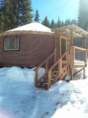 Una iurta amb un porxo de fusta i una finestra, envoltada per la neu.