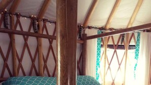Un lit simple avec un cadre en bois et du linge de lit blanc, un plafond en bois et une fenêtre avec des rideaux.