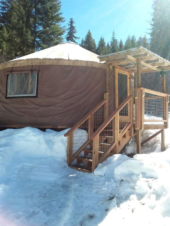 A yurt with a wooden porch and a window, surrounded by snow.