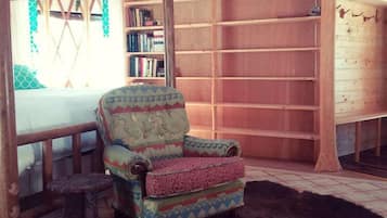 A yurt interior with a patterned armchair, a bookshelf, and a wooden table.