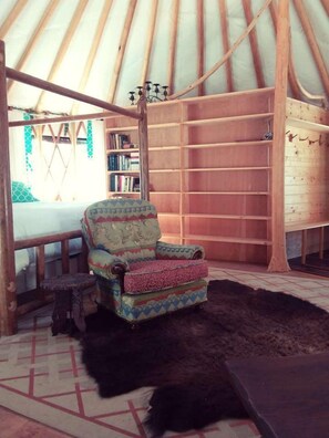 A yurt interior with a patterned armchair, a bookshelf, and a wooden table. - Sanctuary Yurt Glamping Forest Getaway in Alberton, MT (Alberton)