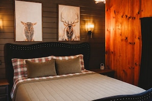Een bed met geruite beddengoed, een donkere hoofdbord en twee aan de muur hangende schilderijen van herten.
