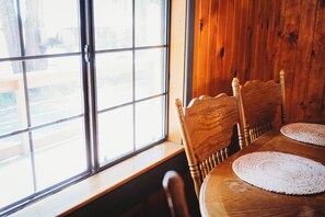 A wooden dining table with four chairs, a window with a view, and a wooden wall. - Bigfoot Alley | Movie Room + Walkable Location (Shaver Lake)