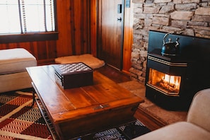A cozy room with a wooden coffee table, a fireplace, and a stone wall. - Bigfoot Alley | Movie Room + Walkable Location (Shaver Lake)