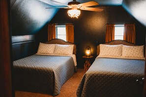 Une chambre avec deux lits, un ventilateur de plafond, une lampe fixée au mur et une fenêtre avec des rideaux.