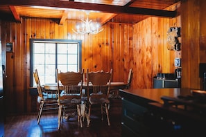 Een houten interieur met een eettafel, stoelen, een kroonluchter en een raam.