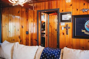 Een kamer met houten lambrisering, een bed, een lijst met een afbeelding en een deur naar een andere kamer.