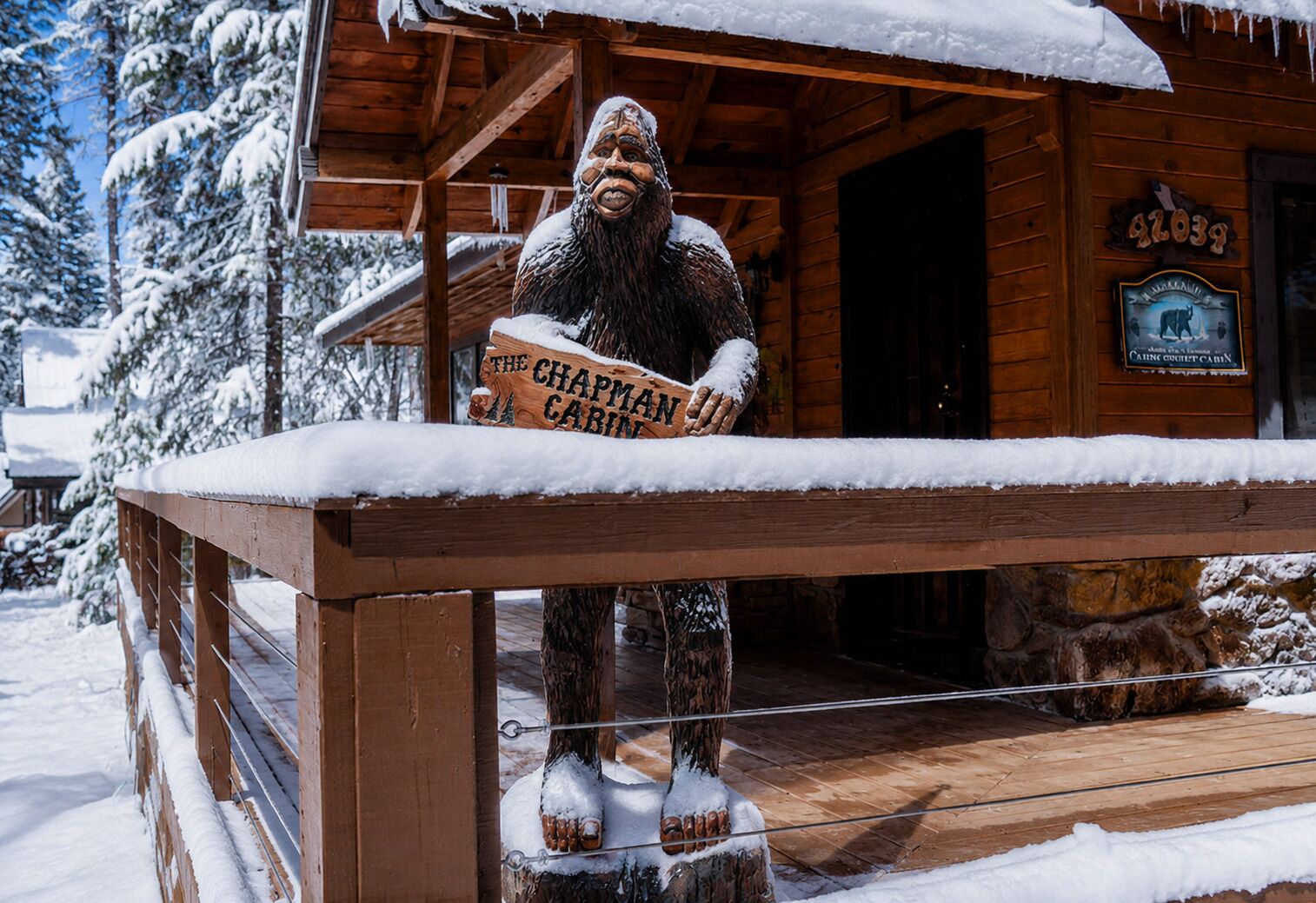 A wooden cabin with a sign reading 'The Chapman Cabin' and a wooden figure holding a sign.