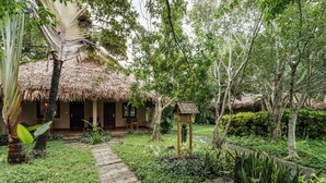 A tropical garden with a thatched-roof structure, a stone pathway, and lush greenery. - Cuc Phuong Mineral Retreat (Cuc Phuong)