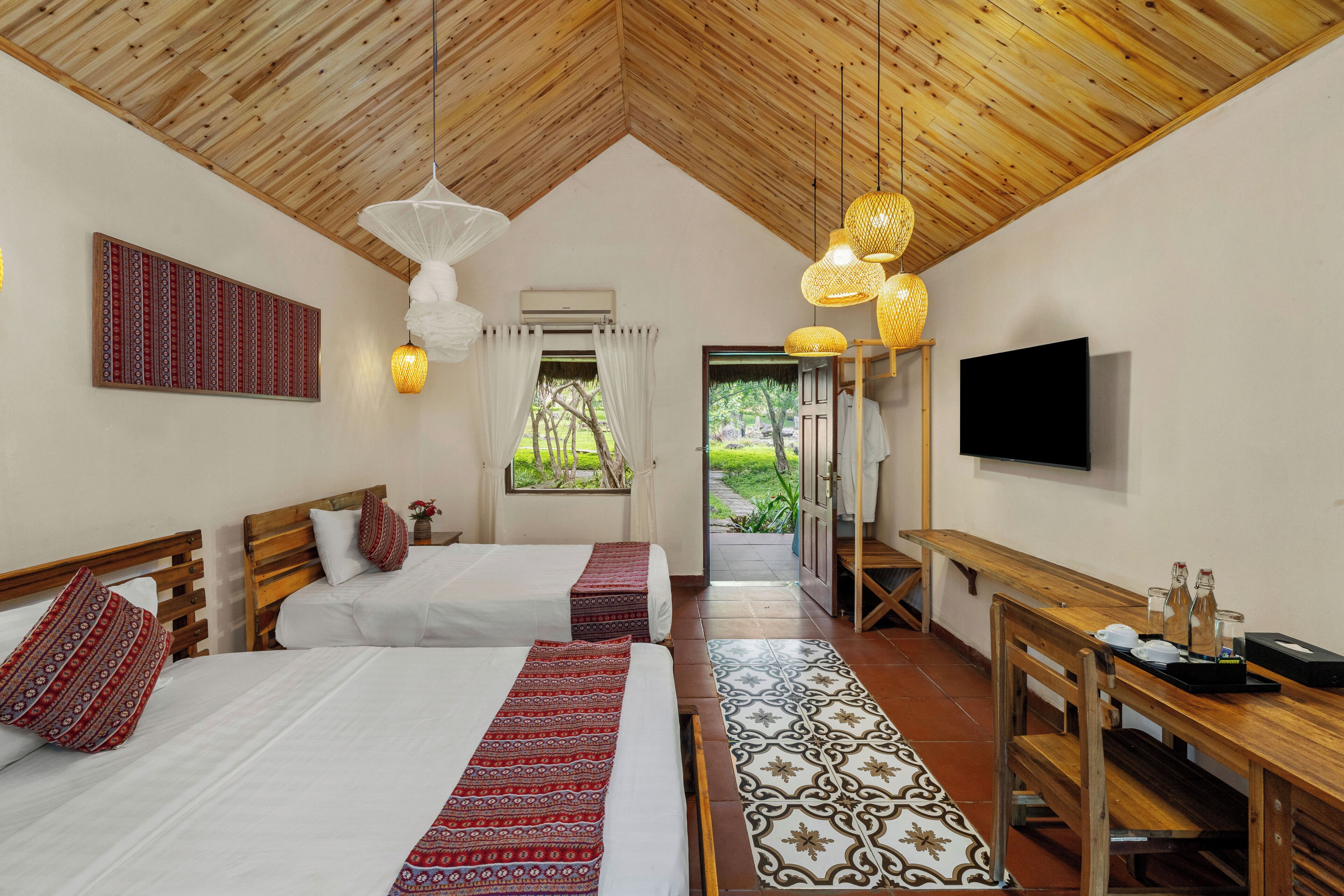 A room with two beds, a TV, a wooden bench, and a patterned rug.
