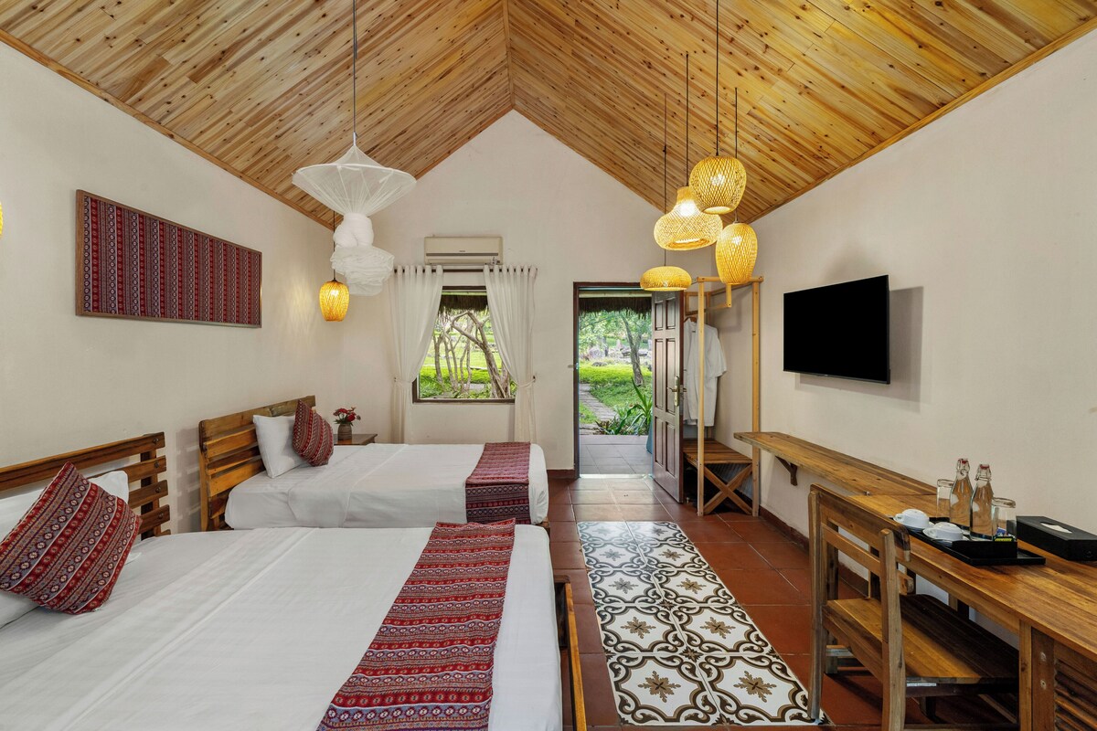 Una habitación con dos camas, televisión, banco de madera y alfombra estampada.