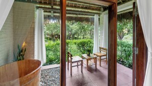 A wooden-framed glass door leading to a patio with a wooden table and chairs, a wooden tub, and a view of a lush garden. - Cuc Phuong Mineral Retreat (Cuc Phuong)