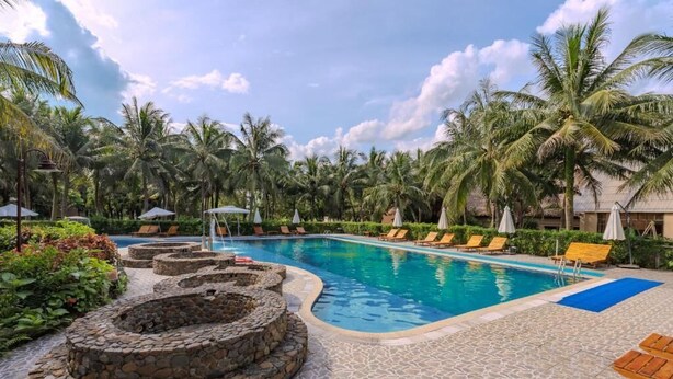 A pool area with lounge chairs, palm trees, and a stone fire pit. - Cuc Phuong Mineral Retreat (Cuc Phuong)