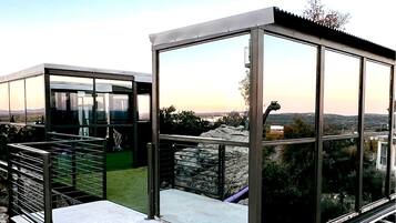 A modern glass structure with a metal railing, a stone wall, and a view of the landscape.