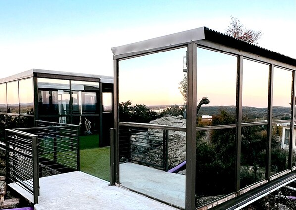 A modern glass structure with a metal railing, a stone wall, and a view of the landscape.