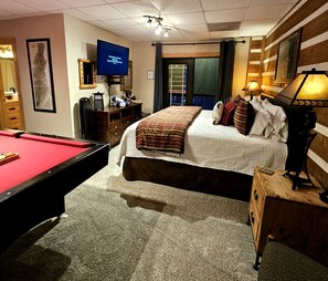 Quarto de hotel com mesa de bilhar, cama com manta xadrez, televisão e abajur.