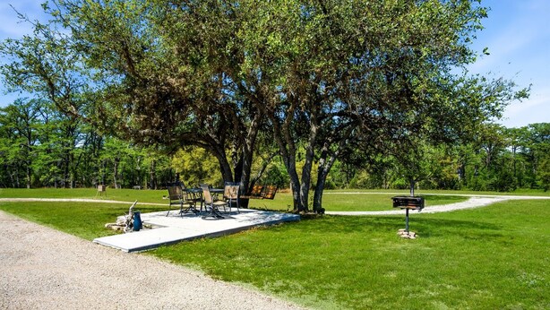 A park with a picnic table, chairs, a grill, and a signpost. - Charming Riverside Cabin Escape with Outdoor Relaxation Spaces in Medina, Texas (Medina)