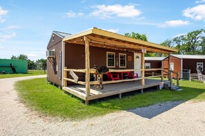 Ein rustikales Blockhaus mit Veranda, einer kleinen Sitzgelegenheit im Freien und einem Kiesweg, der dorthin führt.