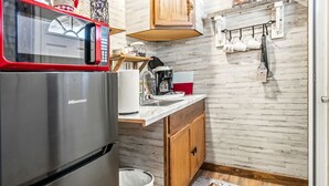 A compact kitchen with a stainless steel refrigerator, a microwave, a coffee maker, and wooden cabinets. - Charming Riverside Cabin Escape with Outdoor Relaxation Spaces in Medina, Texas (Medina)