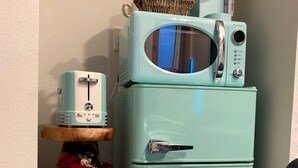 A teal vintage refrigerator with a microwave on top, a wooden shelf with a vase and red flowers, and a small toaster. - Unique Container Escape with Panoramic Hilltop Views in Cottonwood Shores, Texas (Cottonwood Shores)