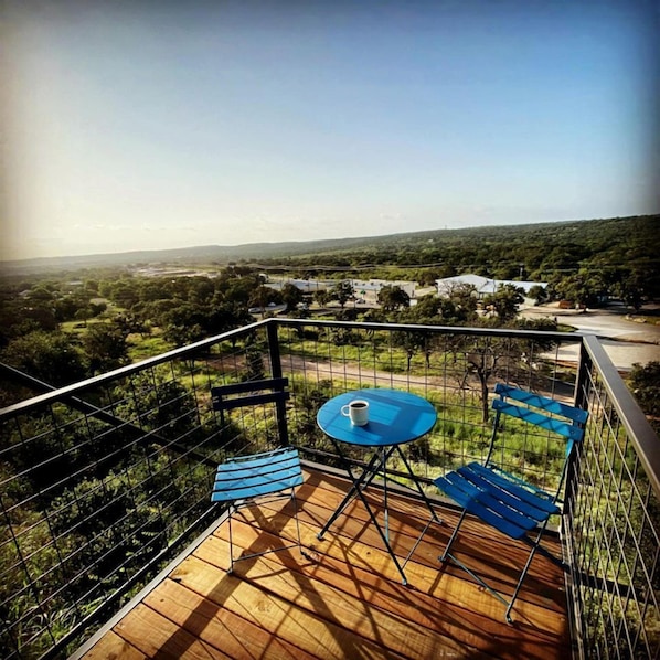 A balcony with a table and chairs, overlooking a landscape with trees and buildings.