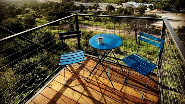 Uma varanda com mesa e cadeiras, com vista para uma paisagem com árvores e edifícios.