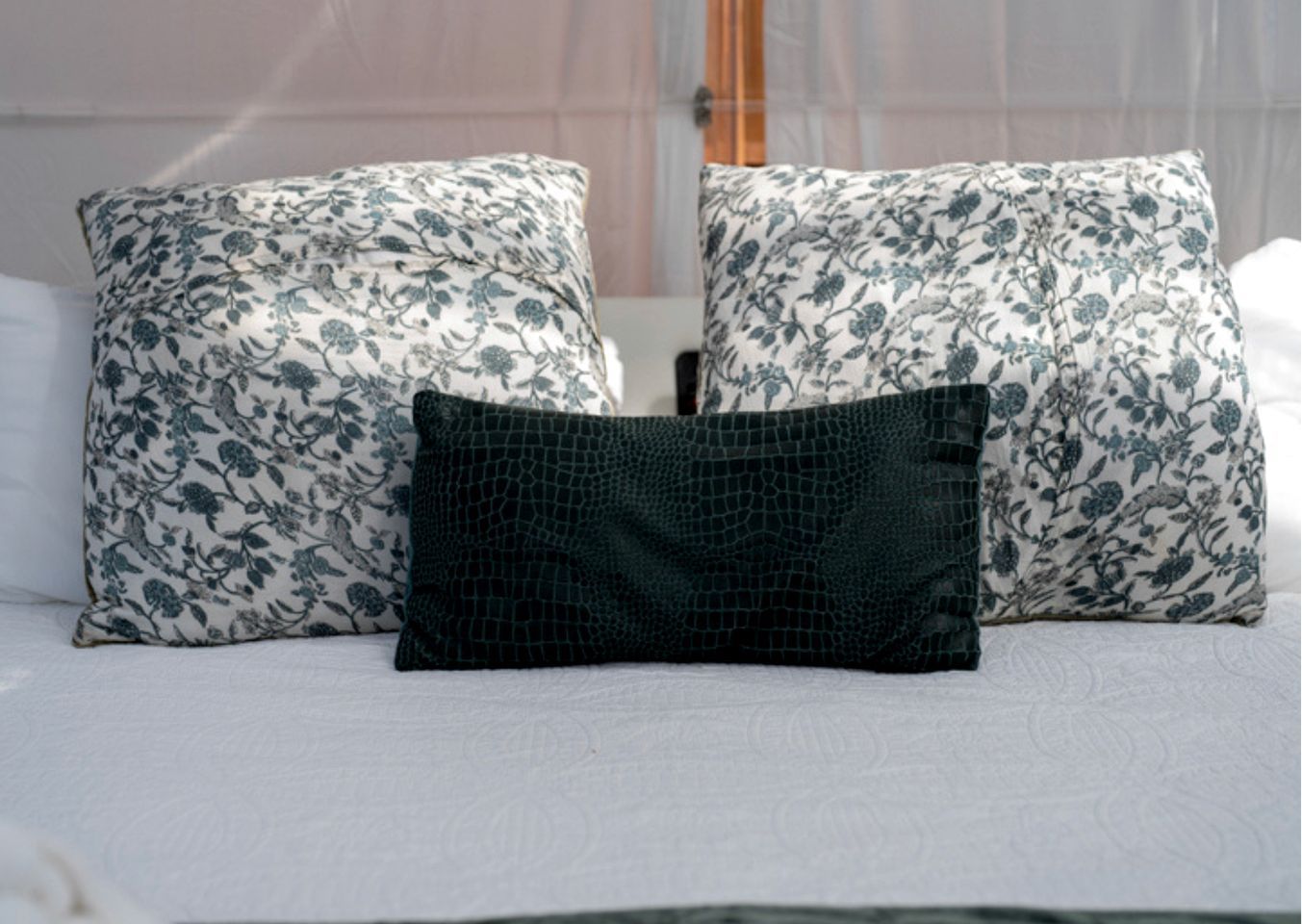 Un lit avec deux oreillers à motifs floraux et un seul oreiller à texture particulière.