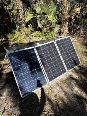 Three solar panels on the ground with a natural background.