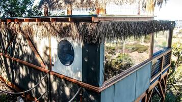 A thatched-roof structure with a circular window, wooden railings, and a rope barrier.