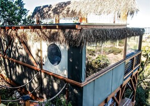 A thatched-roof structure with a circular window, wooden railings, and a rope barrier.