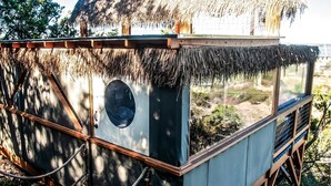 A thatched-roof structure with a circular window, wooden railings, and a rope barrier.