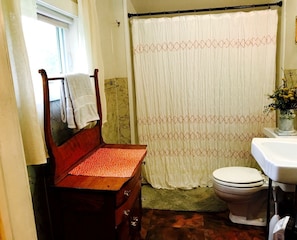 Ein Badezimmer mit einer hölzernen Sitzbank, Toilette, Waschbecken und einer Duschvorhang.