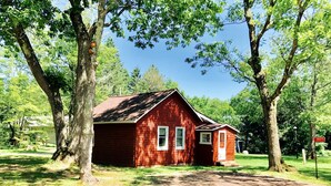 A red wooden cabin with a small porch, surrounded by trees and a clear sky. - Charming Lakeside Cabin Rental near Camp Nine Pines, Wisconsin (Ashland)