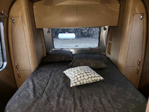 Ein kompaktes Wohnmobil-Interieur mit einem Bett, zwei Kissen, einem Fenster und Stauraumschränken.