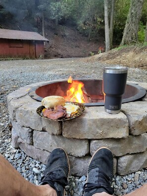 Ein Steinkamin mit einem YETI-Becher, einem Teller mit Essen und den Füßen einer Person.