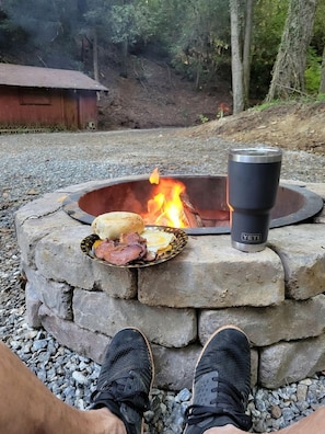 Ein Steinkamin mit einem YETI-Becher, einem Teller mit Essen und den Füßen einer Person.