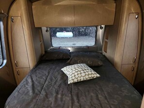 Ein kompaktes Wohnmobil-Interieur mit einem Bett, zwei Kissen, einem Fenster und Stauraumschränken.