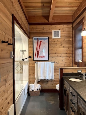 Ein Badezimmer mit Holzwandverkleidung, einer Dusche, einem Waschbecken und einem gerahmten Poster an der Wand.