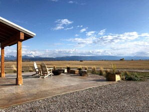 Eine überdachte Terrasse mit Adirondack-Stühlen, einer Feuerstelle und Blick auf ein Gebirge.