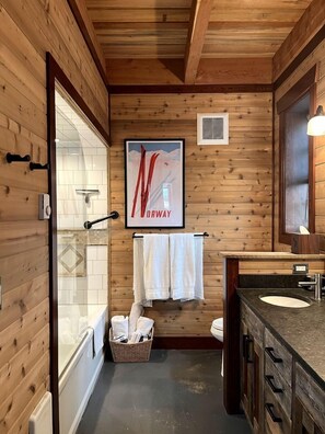 Ein Badezimmer mit Holzwandverkleidung, einer Dusche, einem Waschbecken und einem gerahmten Poster an der Wand.