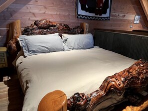 Ein hölzernes Bett mit geschnitztem Kopfteil und Fußteil, einem gestreiften Kopfkissen und einer schlichten Bettdecke.