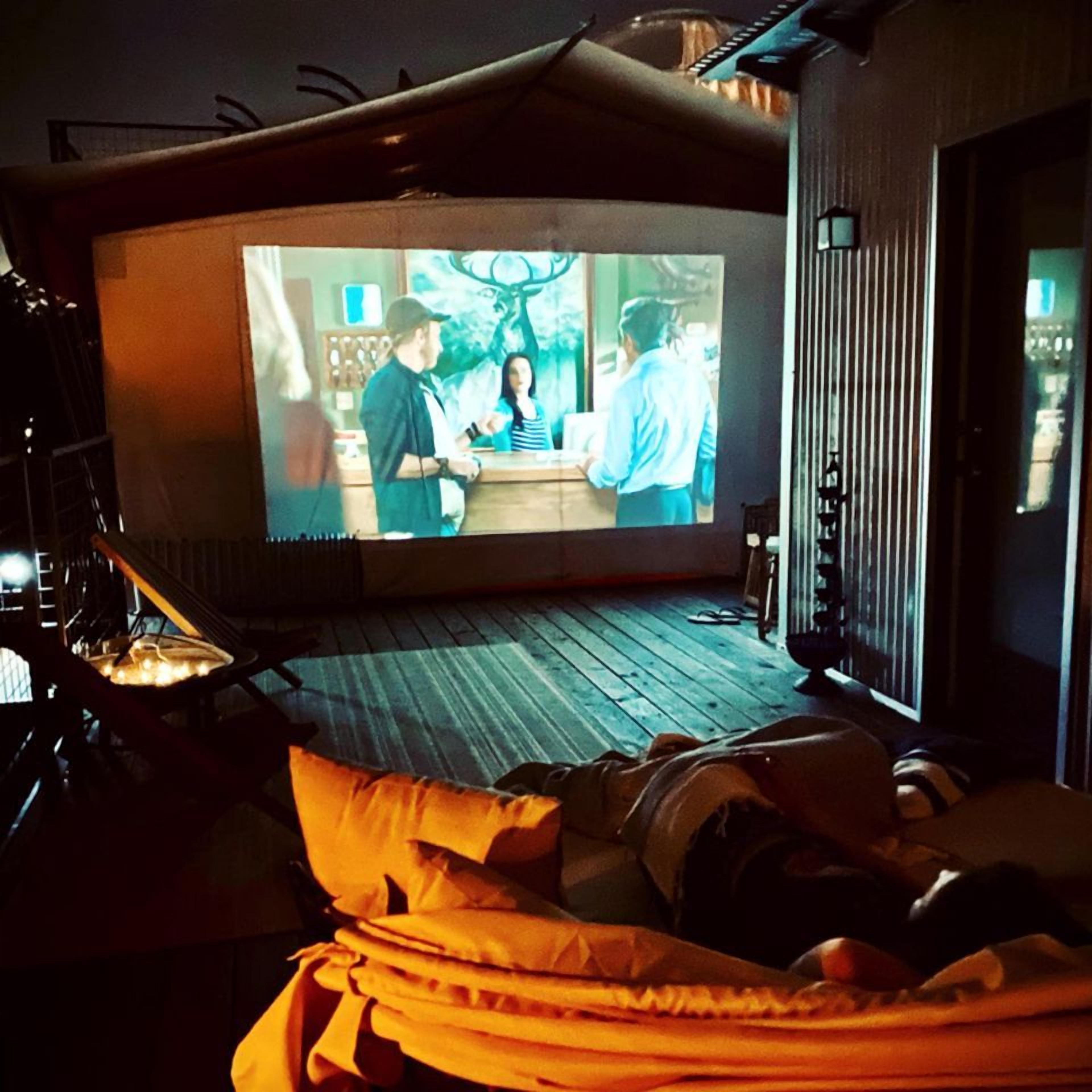 Ett mysigt rum med en stor skärm för att titta på film eller tv, en bekväm sittgrupp och ett trägolv.