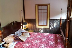 Ein Schlafzimmer mit Himmelbett, Holz-Kopfstütze, Fenster mit Gittermuster und einer Nachttischlampe.
