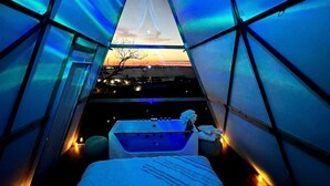 Una habitación con cama, bañera y vistas al atardecer a través de una ventana triangular.