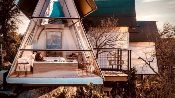 Una estructura de cúpula geodésica con piso transparente, balcón y vista de un edificio al fondo.