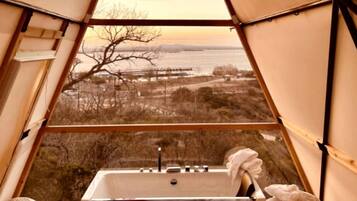 A tent with a bathtub, a view of the landscape, and a window.