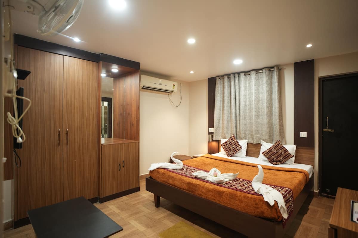 A hotel room with a bed, wooden wardrobe, air conditioning unit, and a desk.