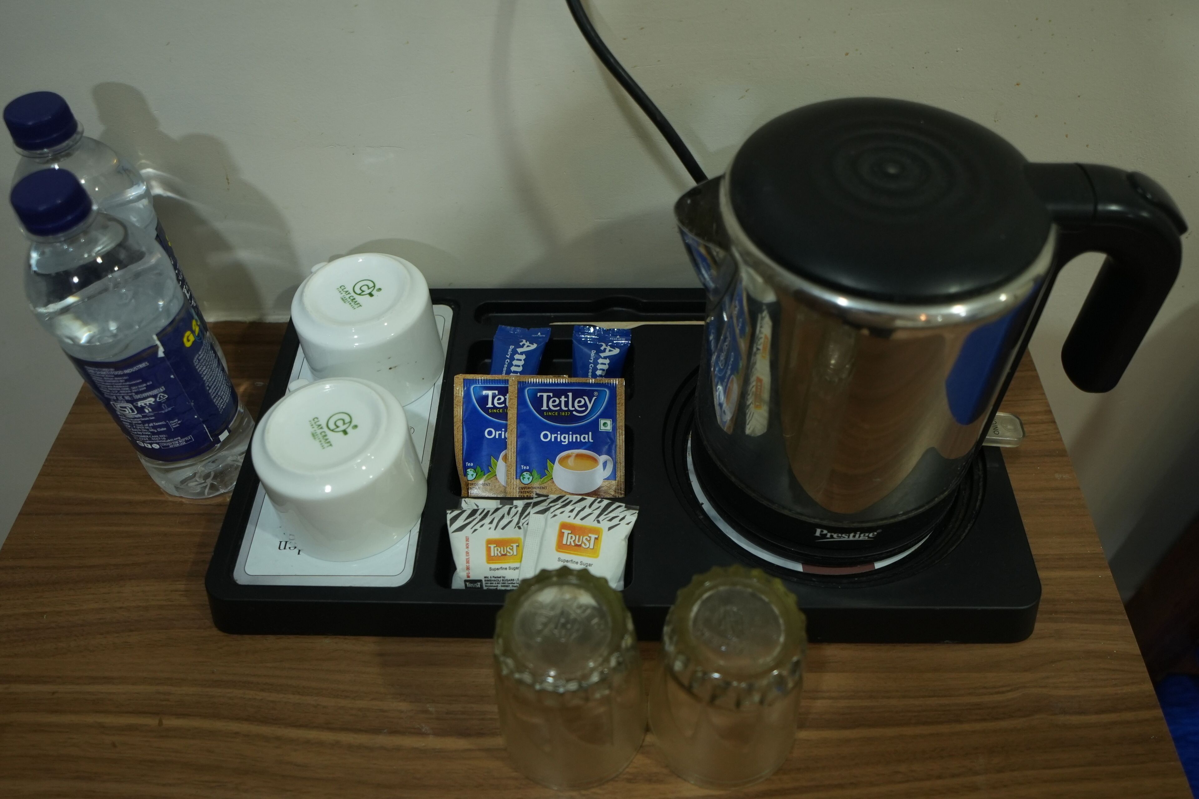 A coffee maker, two bottles of water, a white cup, and packets of coffee on a wooden surface.