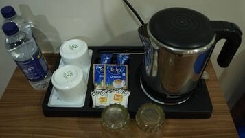 A coffee maker, two bottles of water, a white cup, and packets of coffee on a wooden surface.