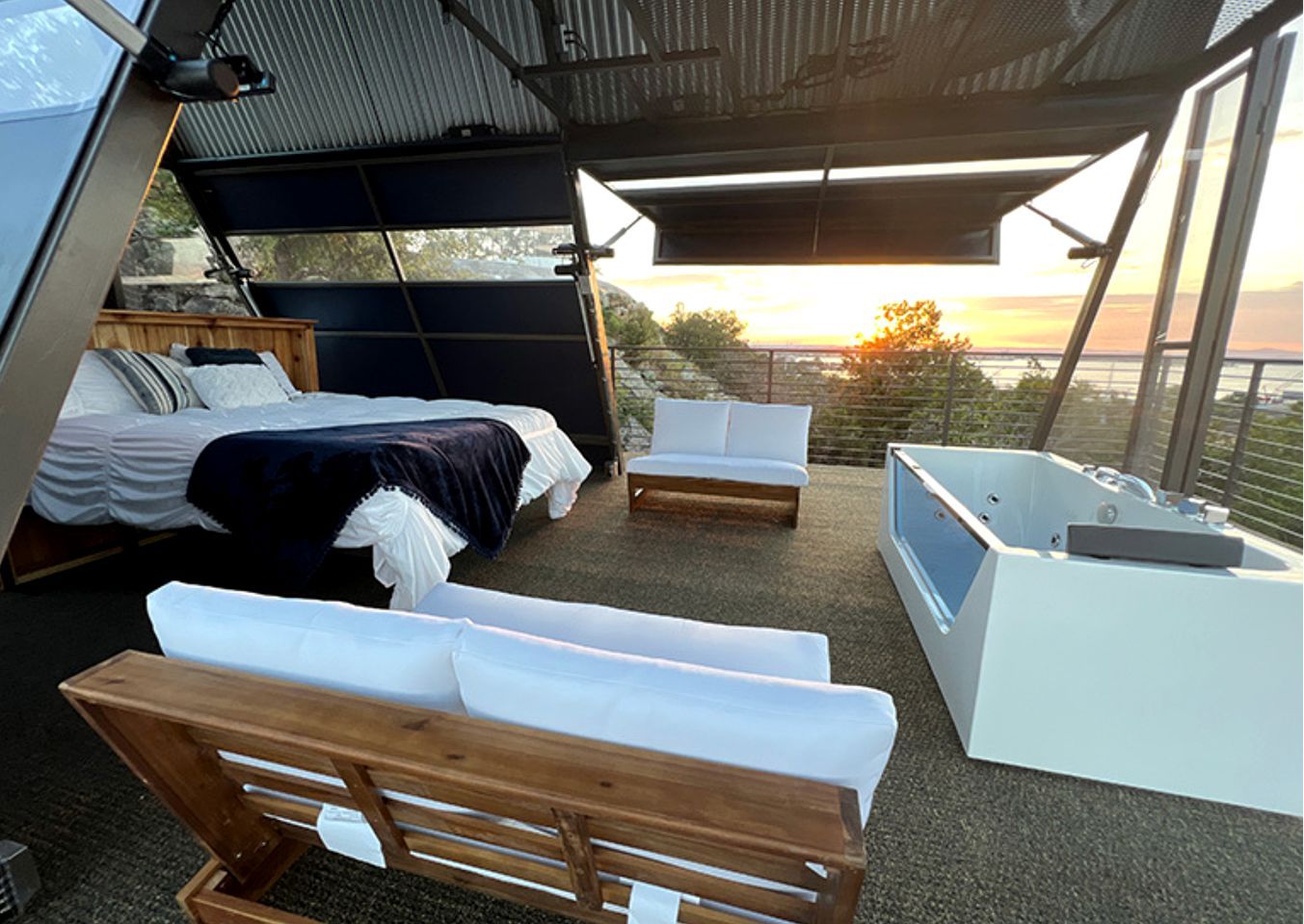 A modern bedroom with a bed, two white sofas, a wooden bench, and a bathtub.